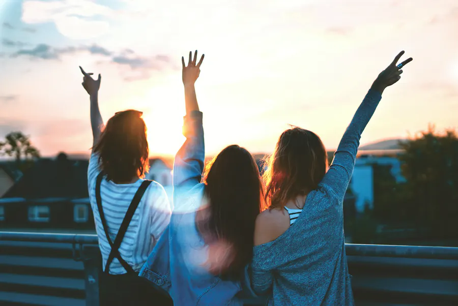 Three friends on a rooftop at sunset, arms raised to the sky